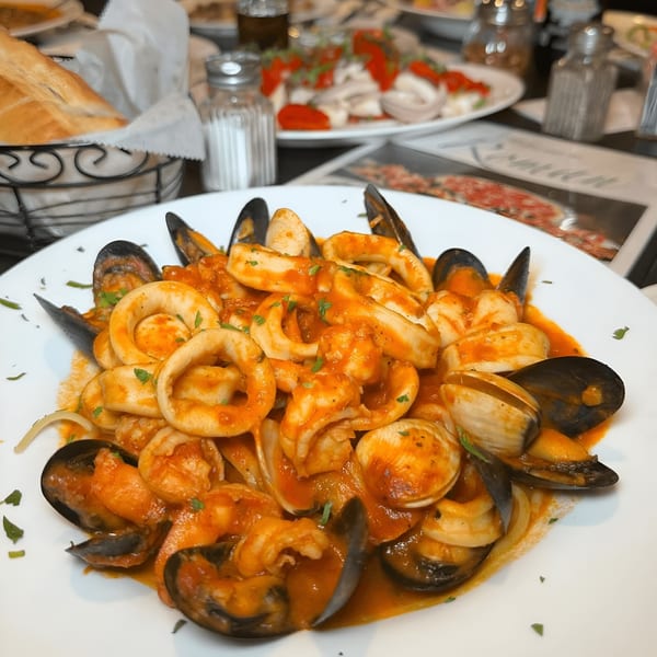 A white plate filled with seafood pasta, including mussels, clams, squid, and shrimp in red sauce.