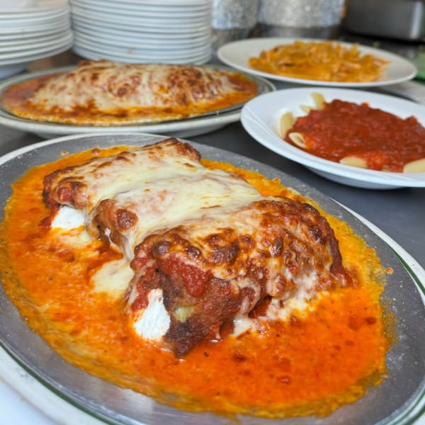 Baked ziti with melted cheese and red sauce, alongside other pasta dishes at Roman Pizza & Restaurant.