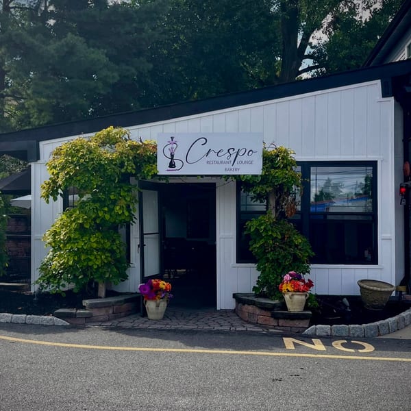 Exterior of Crespo Restaurant Lounge Bakery, a white building with black trim, green foliage, and flower pots.