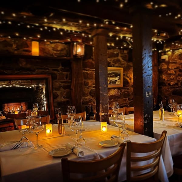 Cozy Roman Pizza & Restaurant dining room with stone walls, string lights, and candlelit tables.