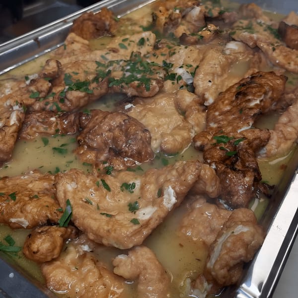 Close-up of golden-brown chicken pieces simmering in a light sauce, garnished with fresh parsley.
