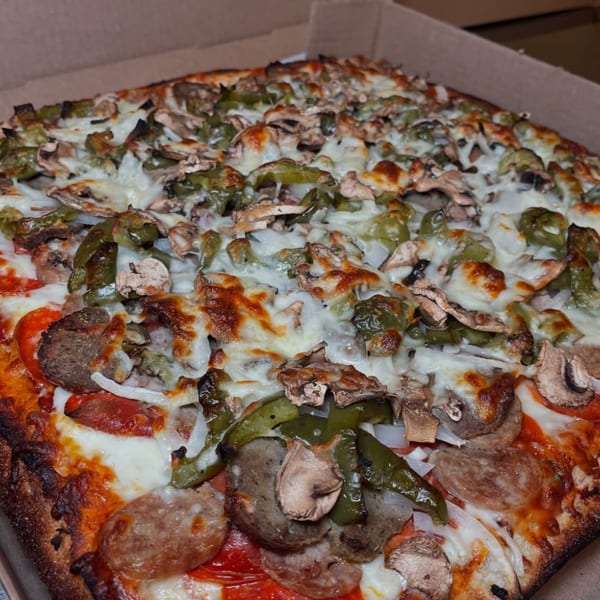 A Roman Pizza & Restaurant pizza with sausage, green peppers, mushrooms, and onions in a box.