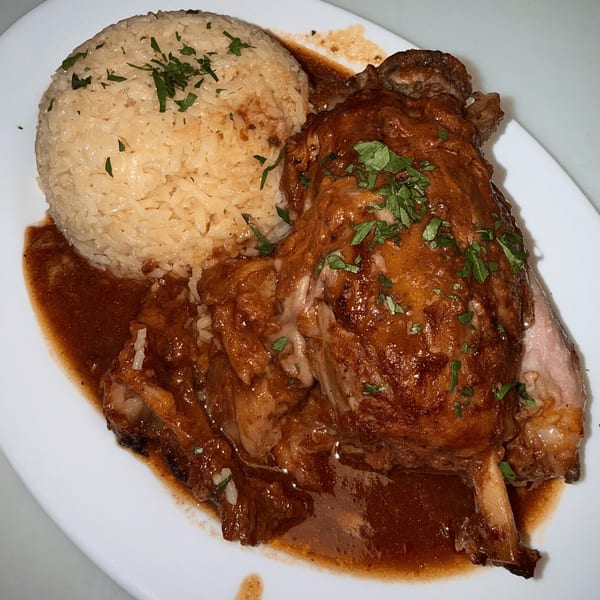 Braised lamb shank with rich brown sauce and a side of white rice, garnished with parsley.