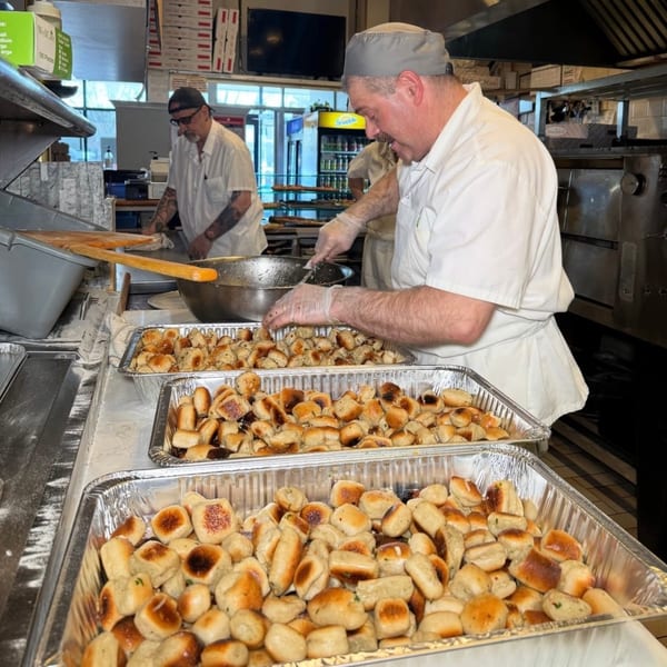 Chefs prepare trays of freshly baked garlic knots in a busy Roman Pizza & Restaurant kitchen.