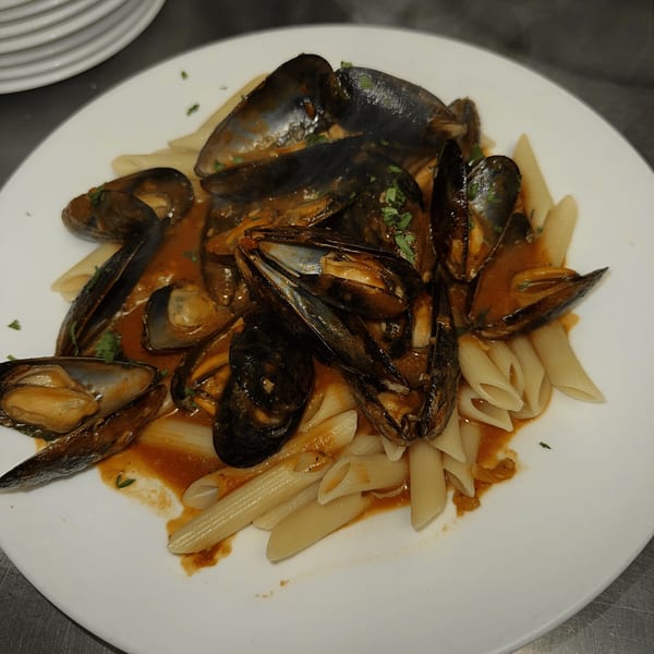 Mussels in a rich red sauce with penne pasta, garnished with fresh herbs on a white plate.