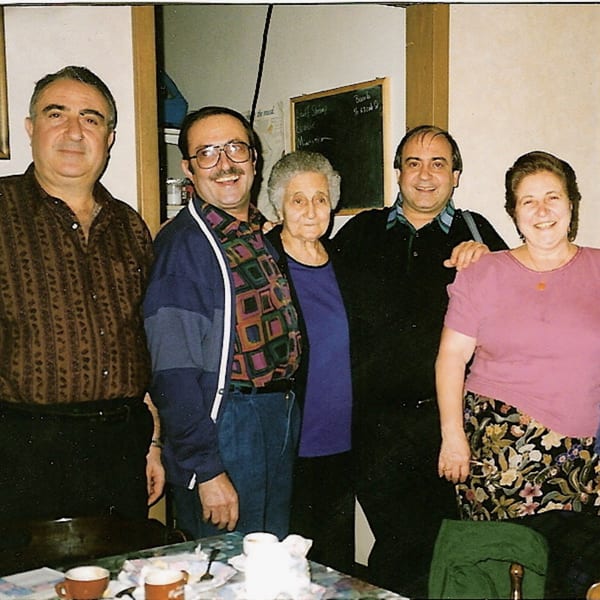 Five smiling people, three men and two women, standing together in a restaurant setting.