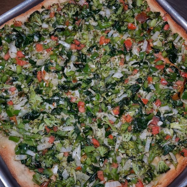 Close-up of a Roman Pizza & Restaurant vegetable pizza, topped with broccoli, spinach, onions, and tomatoes.
