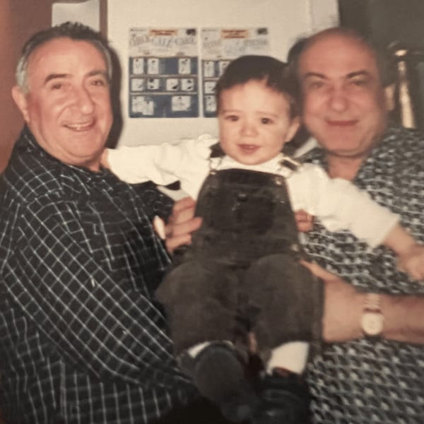 Two smiling men holding a young child in overalls, likely family members at Roman Pizza.