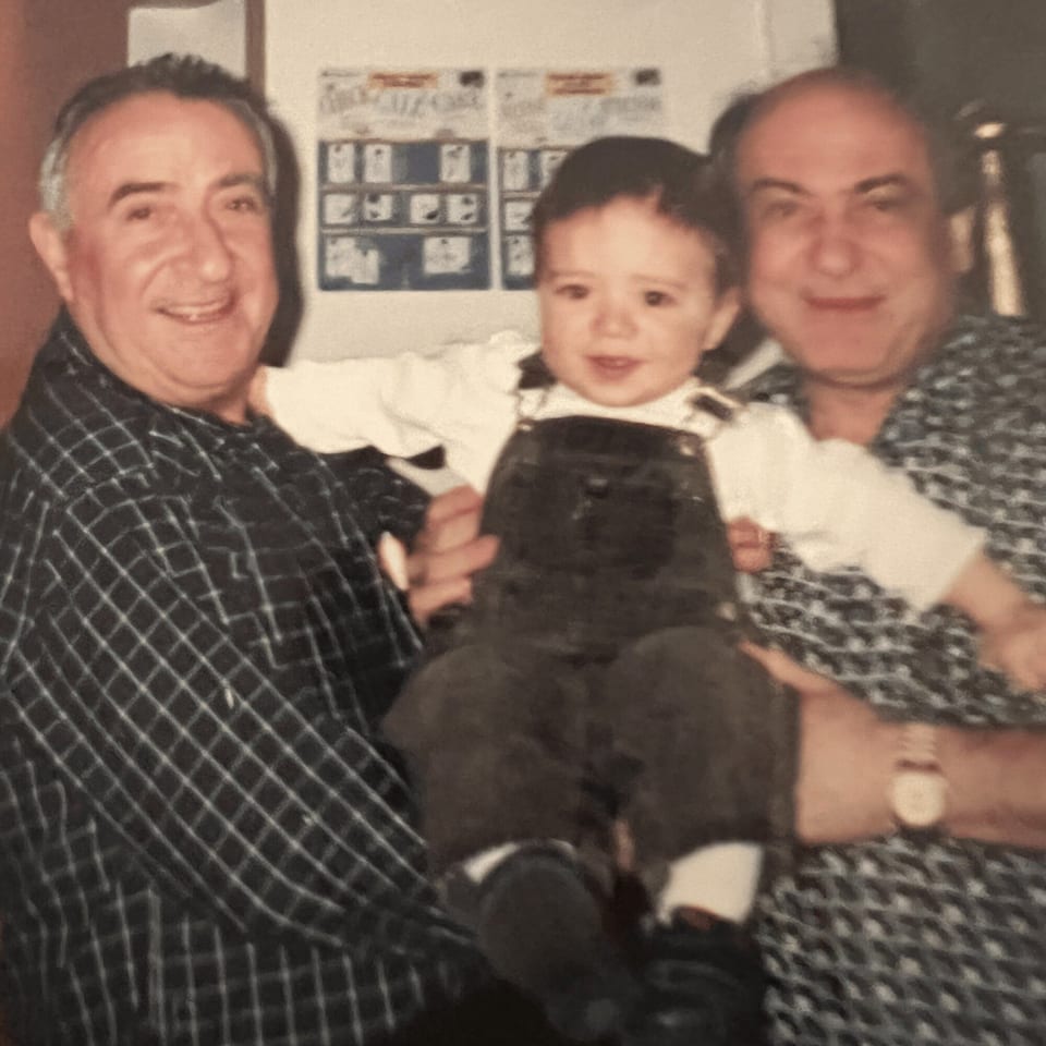Two smiling men holding a young child in overalls, likely family members at Roman Pizza.