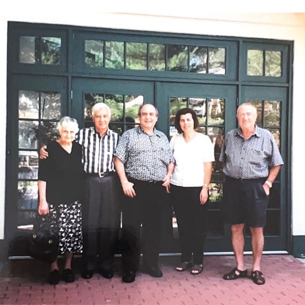 Five people, three men and two women, stand smiling in front of dark green double doors.