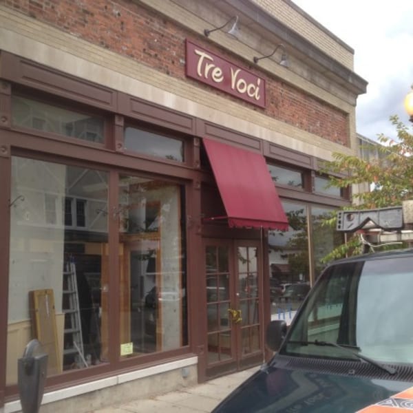 Exterior of Tre Voci restaurant with a red awning, brown trim, and brick facade.