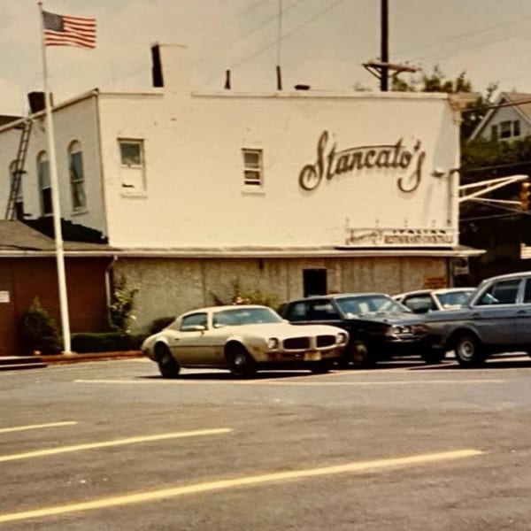 Vintage photo of Stancato's restaurant with an American flag and classic cars in the parking lot.