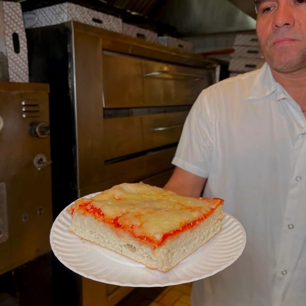 A chef holds a square slice of Roman Pizza's thick-crust pizza with cheese and sauce.