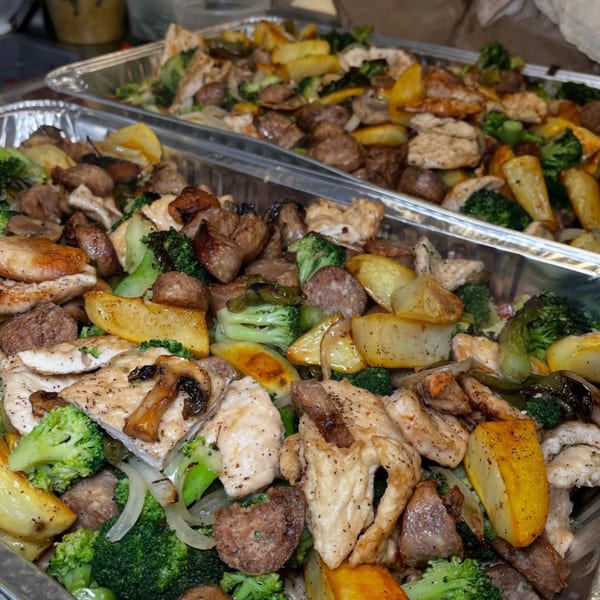 Two foil trays filled with roasted chicken, potatoes, broccoli, mushrooms, and onions.