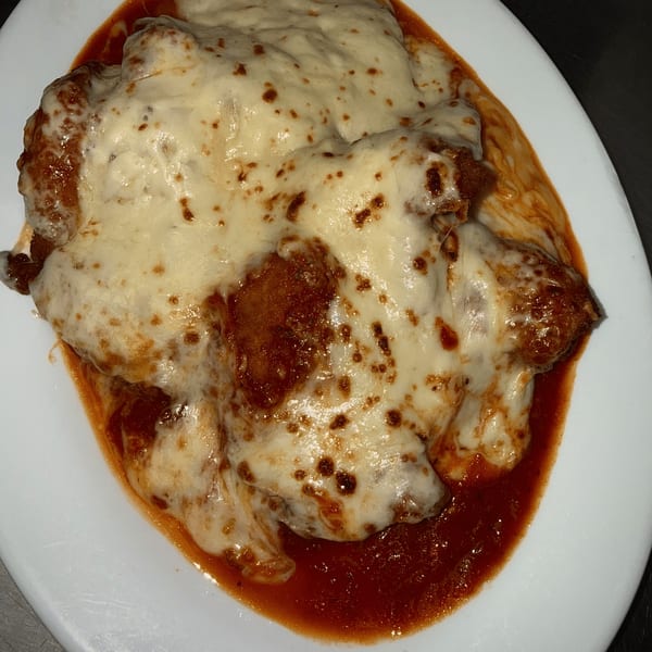 Chicken Parmesan with melted mozzarella cheese and rich red sauce on a white plate.