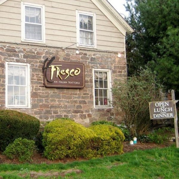 Exterior of Roman Pizza & Restaurant, a stone and siding building with a "Fresco" sign and "Open for Lunch and Dinner" sign.