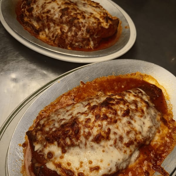 Two baked calzones, topped with melted cheese and rich tomato sauce, on metal plates.