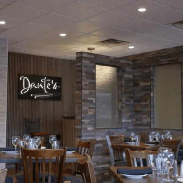 Interior of Roman Pizza & Restaurant with set tables, a "Dante's" sign, and stone wall accents.