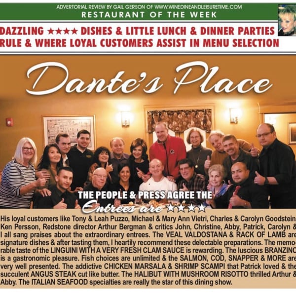 A large group of smiling people, including a chef, posing together in a restaurant dining room.