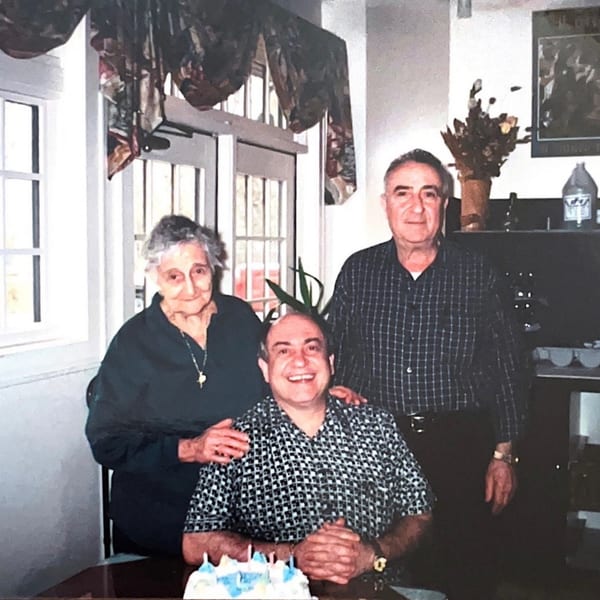 Three generations of the Roman Pizza family smiling, with a birthday cake in the foreground.