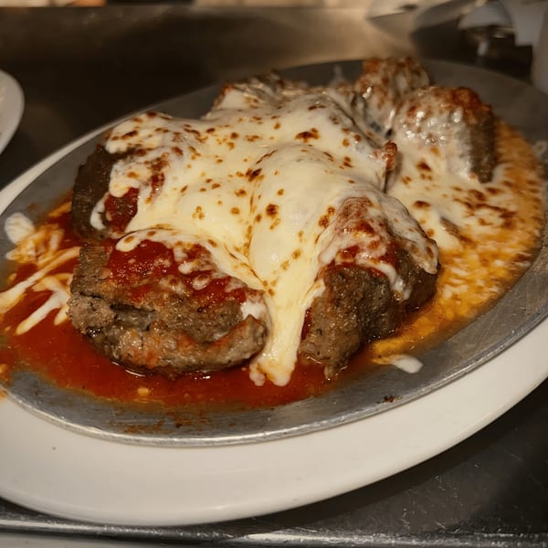 Meatballs covered in melted mozzarella cheese and marinara sauce, served on a metal plate.