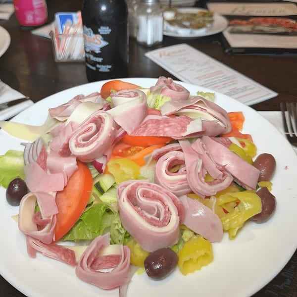 A Roman Pizza & Restaurant antipasto salad with rolled meats, cheese, olives, and vegetables.