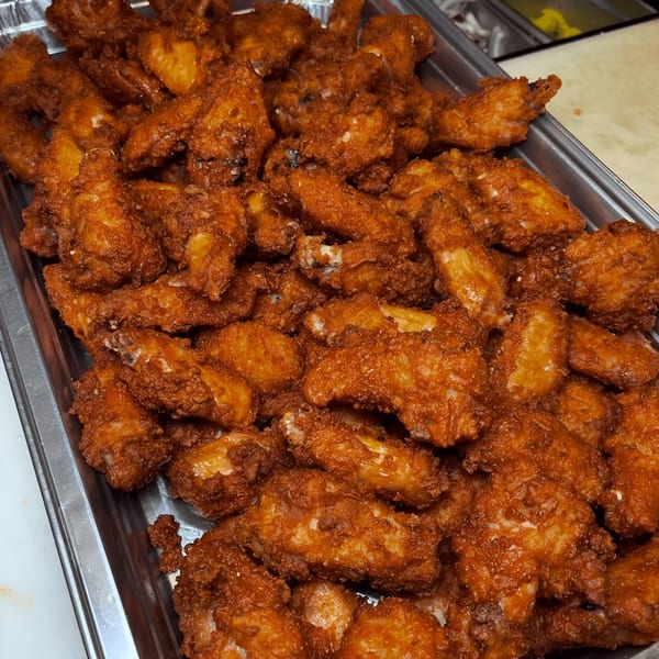 A large metal tray filled with numerous crispy, golden-brown Roman Pizza & Restaurant chicken wings.