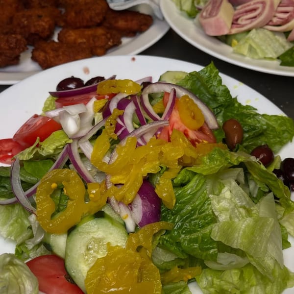 A fresh Roman Pizza & Restaurant house salad with lettuce, tomatoes, onions, cucumbers, olives, and banana peppers.