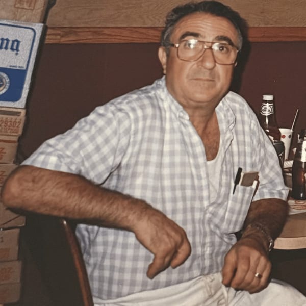 Older man with glasses and a plaid shirt sitting at a table with bottles and boxes.