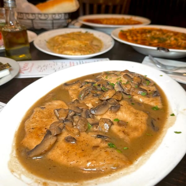 Chicken Marsala with mushrooms and gravy, with other Italian dishes blurred in the background.