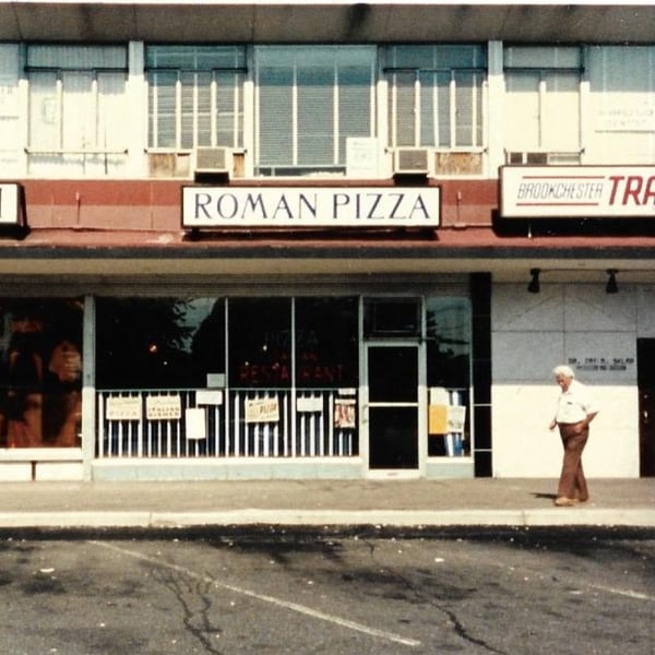 Exterior of Roman Pizza & Restaurant storefront with a person walking by on the sidewalk.