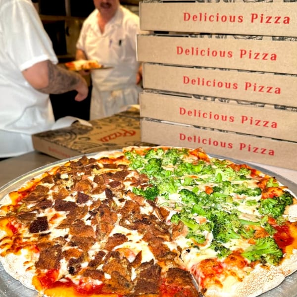 A half-and-half Roman Pizza with meat and broccoli toppings, with pizza boxes and chefs in the background.
