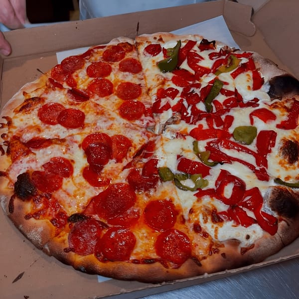 Half pepperoni and half roasted red and green pepper pizza in a Roman Pizza box.