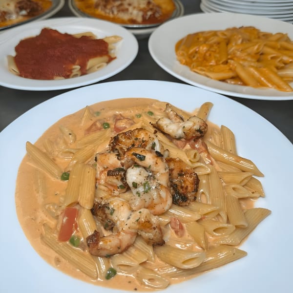 Penne pasta with shrimp in a creamy sauce, with other pasta dishes in the background.