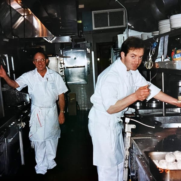 Two chefs in white uniforms working in a busy Roman Pizza & Restaurant kitchen.